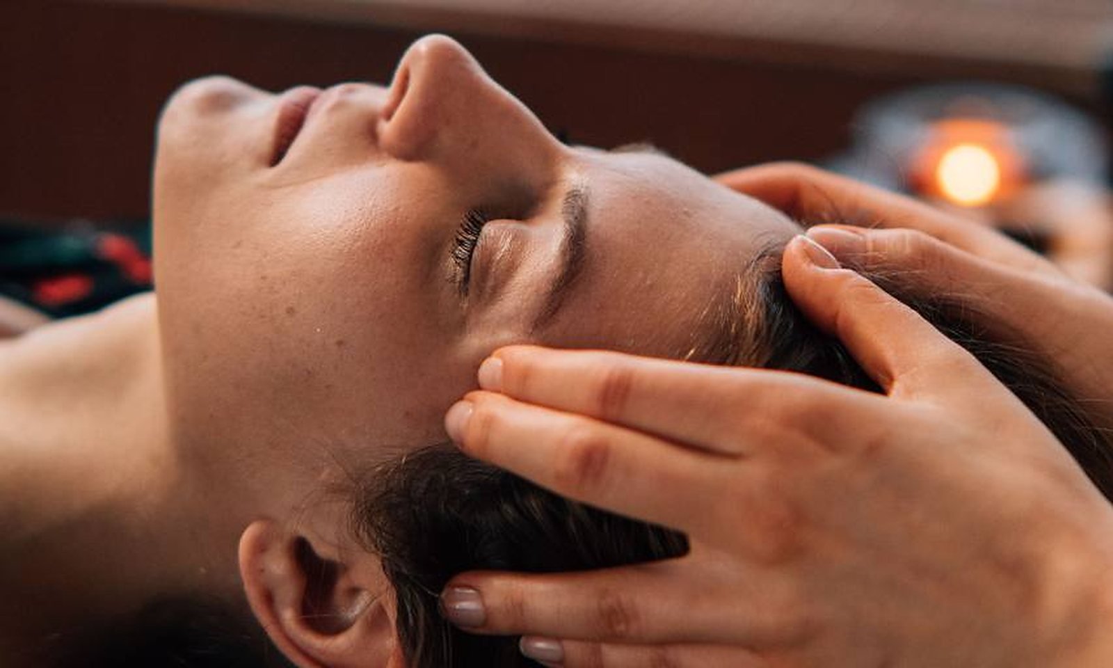 Les mains de la praticienne sur les tempes et le cuir chevelu d'une personne allongée, pendant un massage crânien
