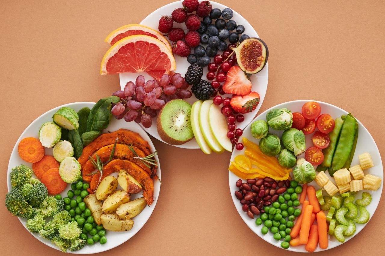 Trois assiettes disposées en triangle : fruits frais, légumes cuits et légumes crus avec des légumineuses, une alimentation riche en micronutriments